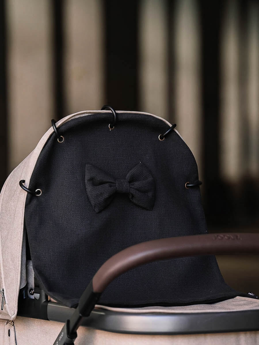 Black waffle pram curtain with a bow attached to a stroller hood