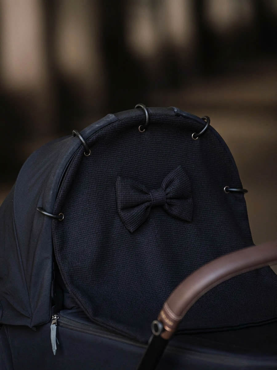 Black waffle pram curtain with a bow attached to a stroller