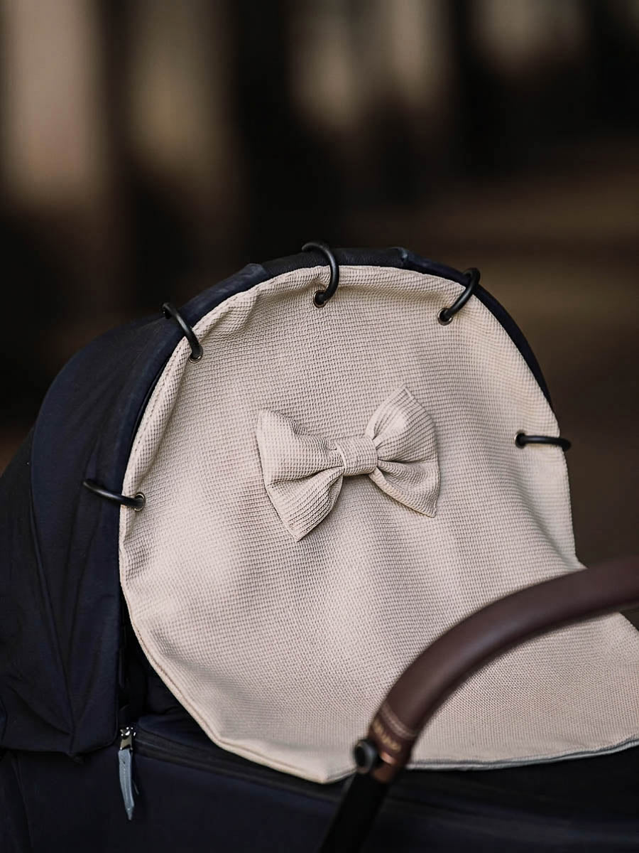 Beige waffle stroller curtain with a bow attached to a pram